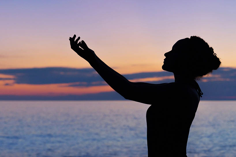 A silhouette of a woman standing against a sunset on the sea.